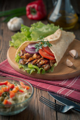Doner kebab is lying on the cutting board. Shawarma with chicken meat, onions, salad lies on a dark old wooden table.