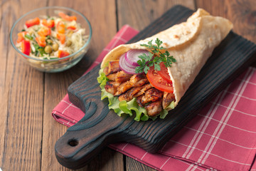 Doner kebab is lying on the cutting board. Shawarma with chicken meat, onions, salad lies on a dark old wooden table.