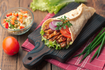 Doner kebab is lying on the cutting board. Shawarma with chicken meat, onions, salad lies on a dark old wooden table.