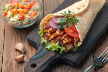 Doner kebab is lying on the cutting board. Shawarma with chicken meat, onions, salad lies on a dark old wooden table.