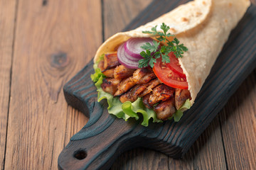 Doner kebab is lying on the cutting board. Shawarma with chicken meat, onions, salad lies on a dark old wooden table.