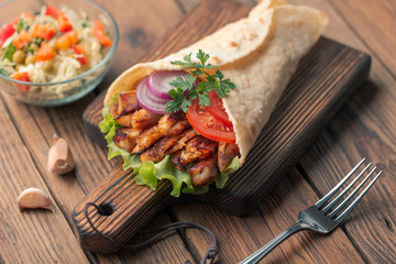 Doner kebab is lying on the cutting board. Shawarma with chicken meat, onions, salad lies on a dark...