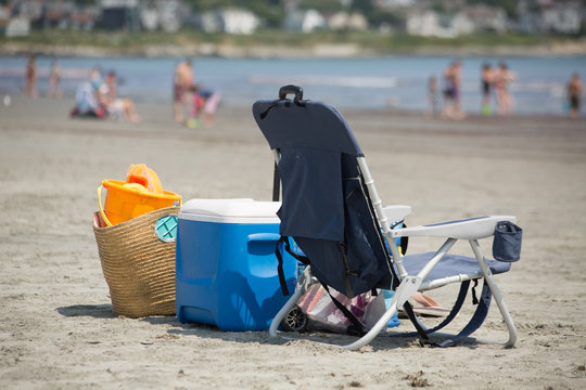 Camp chair, picnic box and a picknic basket on the beach, blurred people in backgraund