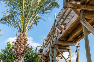 An old wooden construction against a blue sky and palm tree