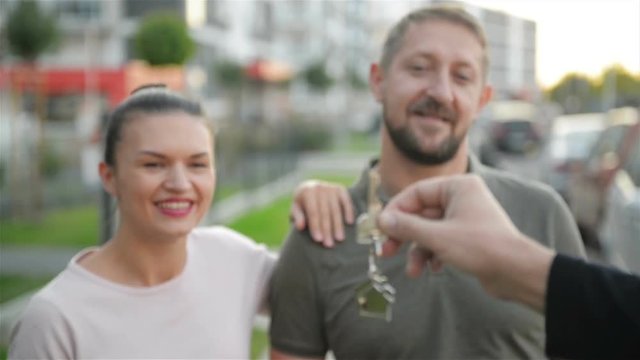 A Hand of Male Real Estate Agent Gives Keys To Owners of New House. Happy Couple.