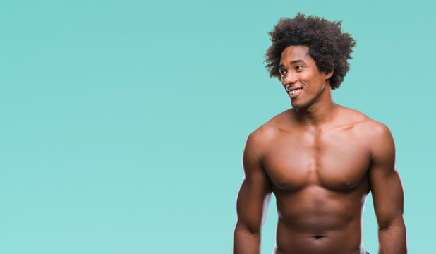 Afro american shirtless man showing nude body over isolated background looking away to side with smile on face, natural expression. Laughing confident.