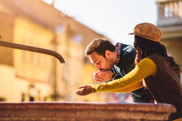 Portrait of beautiful smiling love couple sitting near fountain outdoors in the city. Handsome young man and woman.