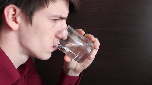 the guy drinks water from a glass cup, in small sips