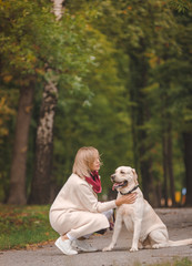 Beautiful young woman walks with her retriever in the park in autumn.