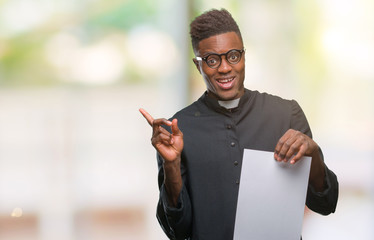 Young african american priest man over isolated background holding blank paper very happy pointing...
