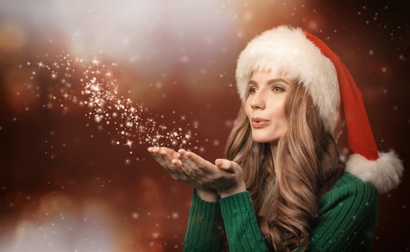 Christmas. Young woman blowing snowflakes from her hands.