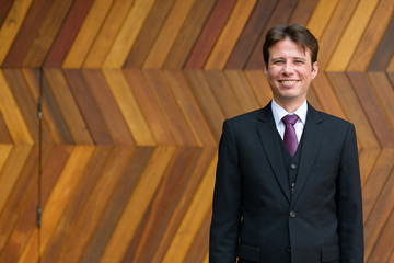 Happy businessman smiling against zigzag patterned wooden wall outdoors