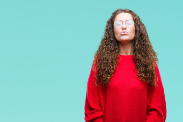 Obraz premium Beautiful brunette curly hair young girl wearing glasses and winter sweater over isolated background puffing cheeks with funny face. Mouth inflated with air, crazy expression.