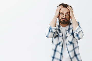 Why me. Portrait of upset and gloomy poor adult man with beard and wrinkles, pursing lips in sad smile, frowning and holding hands on head, being disappointed with bad result of research