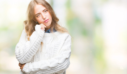 Beautiful young blonde woman wearing winter sweater over isolated background with hand on chin thinking about question, pensive expression. Smiling with thoughtful face. Doubt concept.