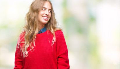 Beautiful young blonde woman wearing winter sweater over isolated background looking away to side with smile on face, natural expression. Laughing confident.