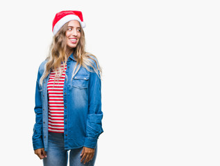 Beautiful young blonde woman wearing christmas hat over isolated background looking away to side with smile on face, natural expression. Laughing confident.