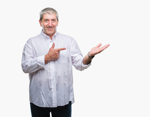 Handsome senior man over isolated background amazed and smiling to the camera while presenting with hand and pointing with finger.