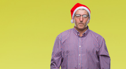 Handsome senior man wearing christmas hat over isolated background with serious expression on face. Simple and natural looking at the camera.