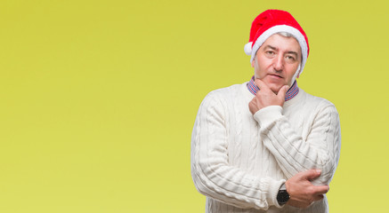 Handsome senior man wearing christmas hat over isolated background looking confident at the camera with smile with crossed arms and hand raised on chin. Thinking positive.