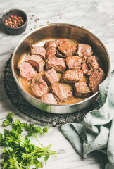 Meat dinner. Braised beef meat stew with fresh parsley in cooking pan over white marble table background. Comfort winter food