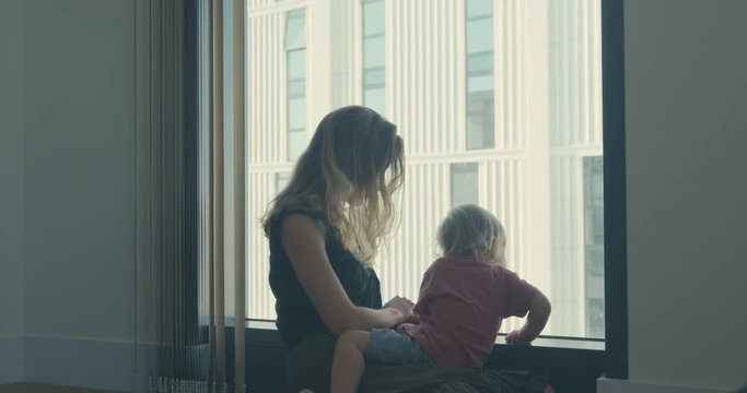 Mother and toddler sitting by the window in high rise