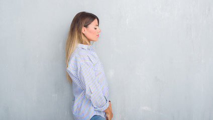 Young adult woman over grey grunge wall wearing fashion business outfit looking to side, relax profile pose with natural face with confident smile.