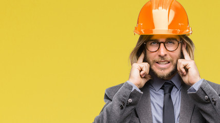 Young handsome architec man with long hair wearing safety helmet over isolated background covering...
