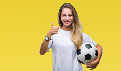 Young beautiful blonde woman holding soccer ball over isolated background happy with big smile doing ok sign, thumb up with fingers, excellent sign