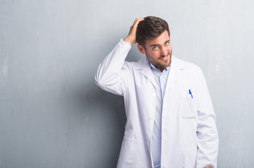 Handsome young professional man over grey grunge wall wearing white coat confuse and wonder about question. Uncertain with doubt, thinking with hand on head. Pensive concept.