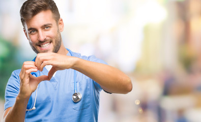 Young handsome doctor surgeon man over isolated background smiling in love showing heart symbol and shape with hands. Romantic concept.