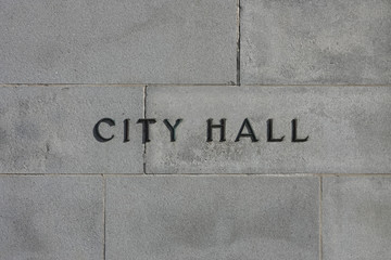 Metal letters reading CITY HALL are shown affixed to a concrete exterior wall of a municipal...