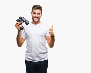 Young handsome man looking through binoculars over isolated background happy with big smile doing ok sign, thumb up with fingers, excellent sign
