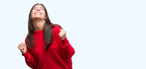 Young beautiful hispanic wearing red sweater very happy and excited doing winner gesture with arms raised, smiling and screaming for success. Celebration concept.