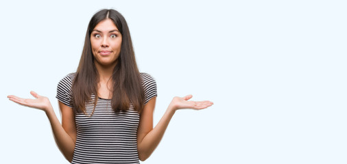Young beautiful hispanic woman clueless and confused expression with arms and hands raised. Doubt...