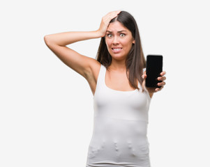 Young beautiful hispanic showing smartphone stressed with hand on head, shocked with shame and surprise face, angry and frustrated. Fear and upset for mistake.