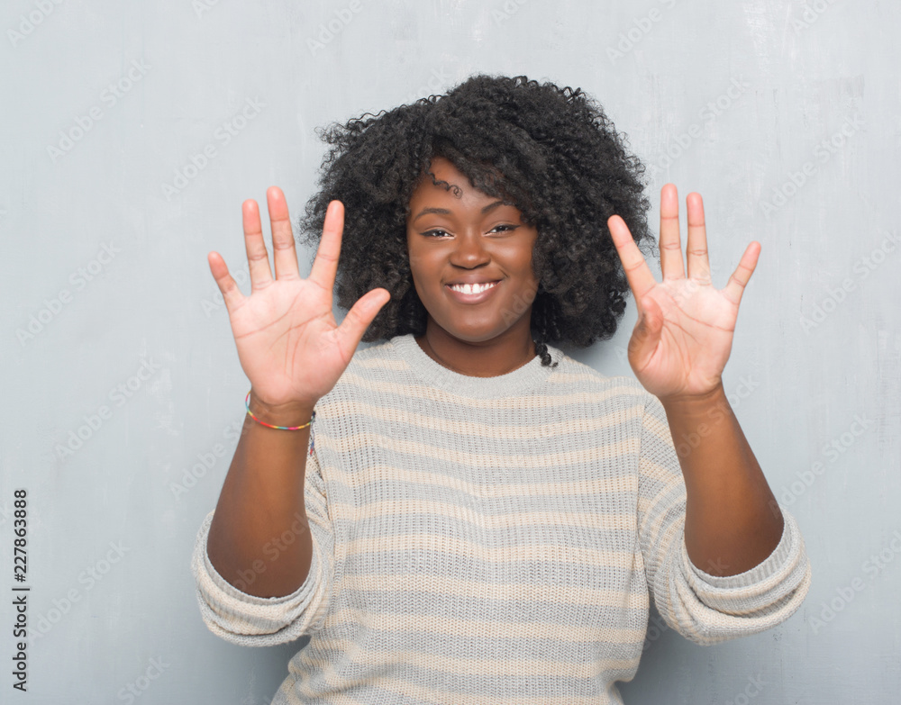 Sticker Young african american plus size woman over grey grunge wall wearing a sweater showing and pointing up with fingers number nine while smiling confident and happy.