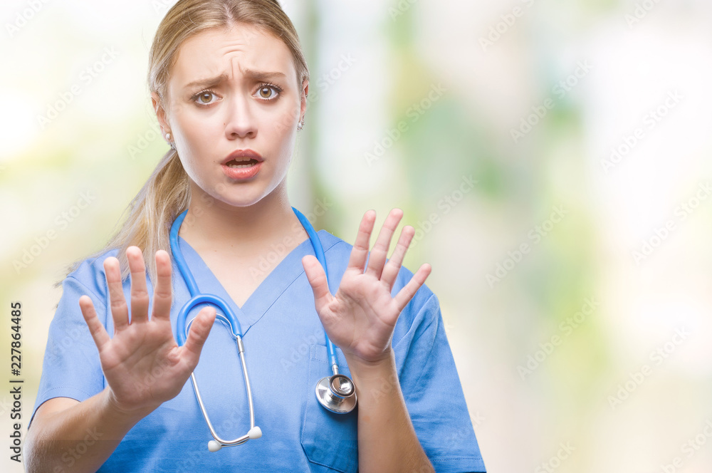 Poster Young blonde surgeon doctor woman over isolated background afraid and terrified with fear expression stop gesture with hands, shouting in shock. Panic concept.