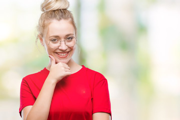 Young blonde woman wearing glasses over isolated background looking confident at the camera with smile with crossed arms and hand raised on chin. Thinking positive.