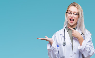 Young blonde doctor woman over isolated background amazed and smiling to the camera while presenting with hand and pointing with finger.