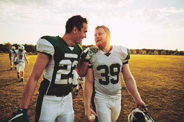 Two smiling American football players walking off a field
