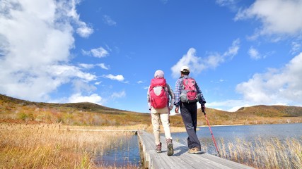 秋空と紅葉の草原を歩く二人