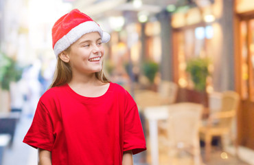 Young beautiful girl wearing christmas hat over isolated background looking away to side with smile on face, natural expression. Laughing confident.
