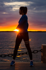 Fototapeta premium An attractive woman in sports clothes doing sports exercises in nature against the sunset and the Amur river