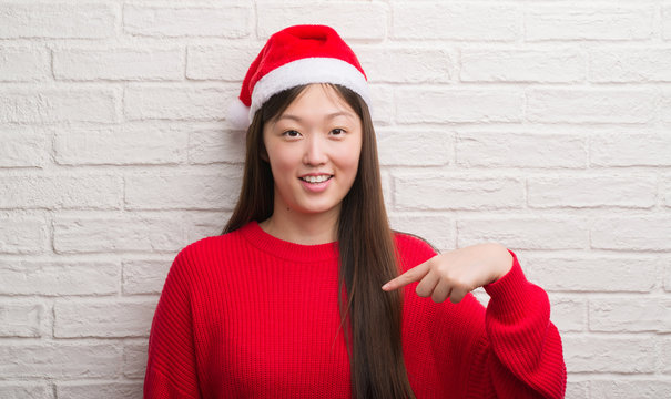 Young Chinese woman wearing Santa Claus hat with surprise face pointing finger to himself