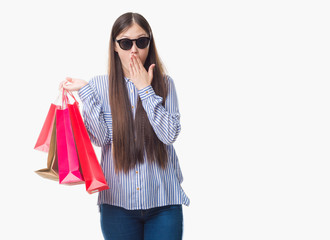 Young Chinese woman over isolated background holding shopping bags on sales cover mouth with hand shocked with shame for mistake, expression of fear, scared in silence, secret concept