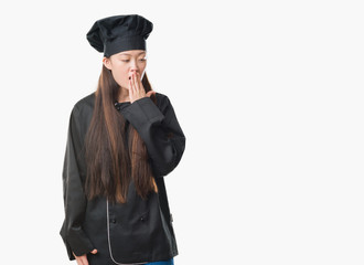 Young Chinese woman over isolated background wearing chef uniform bored yawning tired covering mouth with hand. Restless and sleepiness.