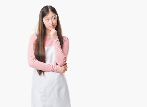 Young Chinese shop owner woman over isolated background wearing white apron serious face thinking about question, very confused idea