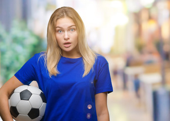 Young caucasian woman holding soccer ball over isolated background scared in shock with a surprise face, afraid and excited with fear expression