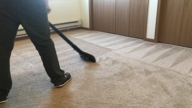Carpet cleaning service professional working brown carpeting in empty apartment room in methodical fashion.